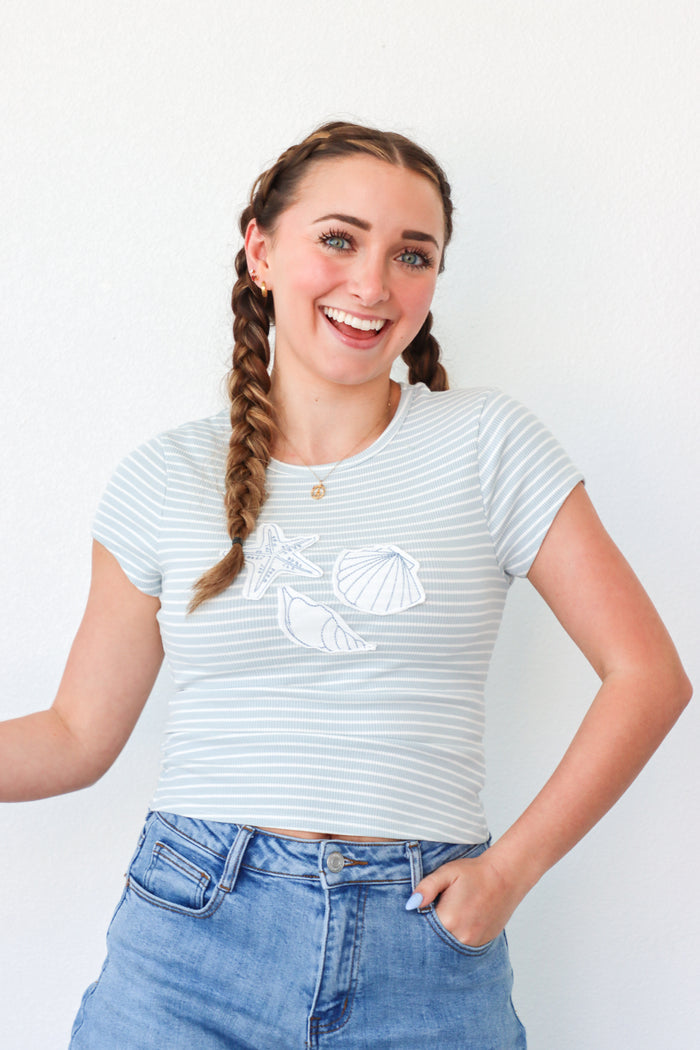 girl wearing light blue stripped t-shirt with seashell patches