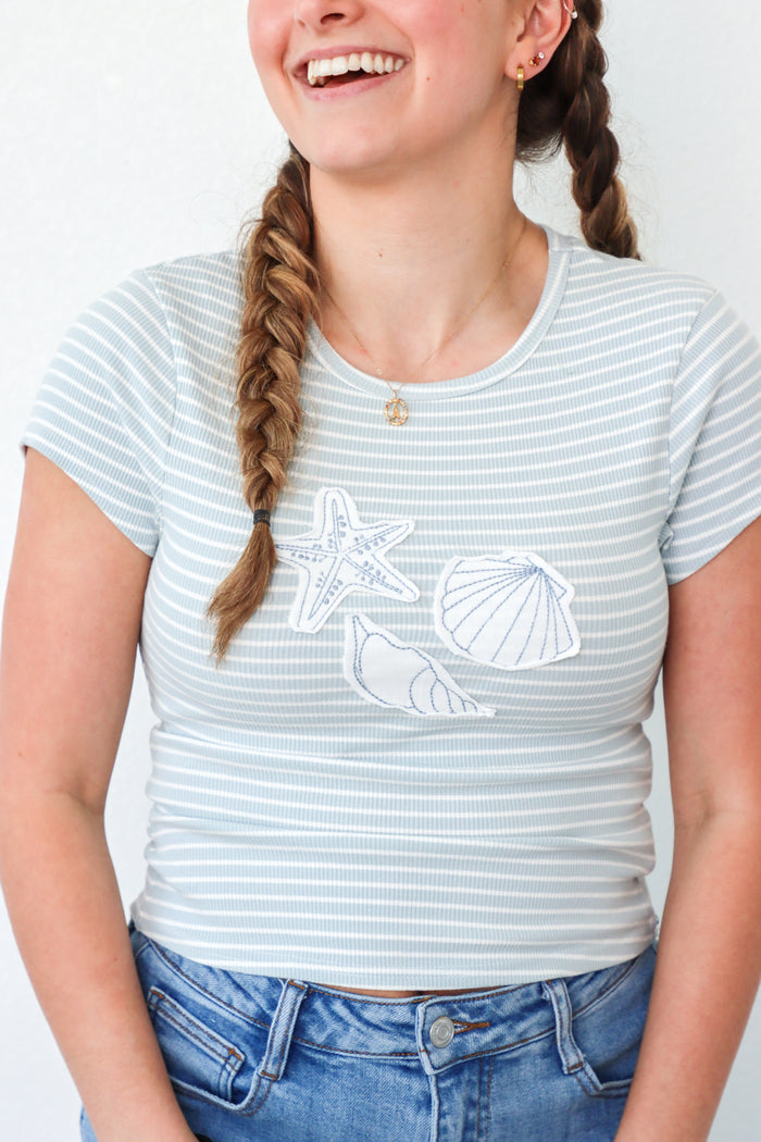girl wearing light blue stripped t-shirt with seashell patches