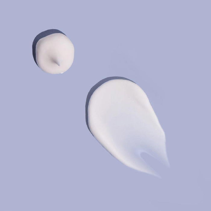 Two drops of white cream on a light purple background.