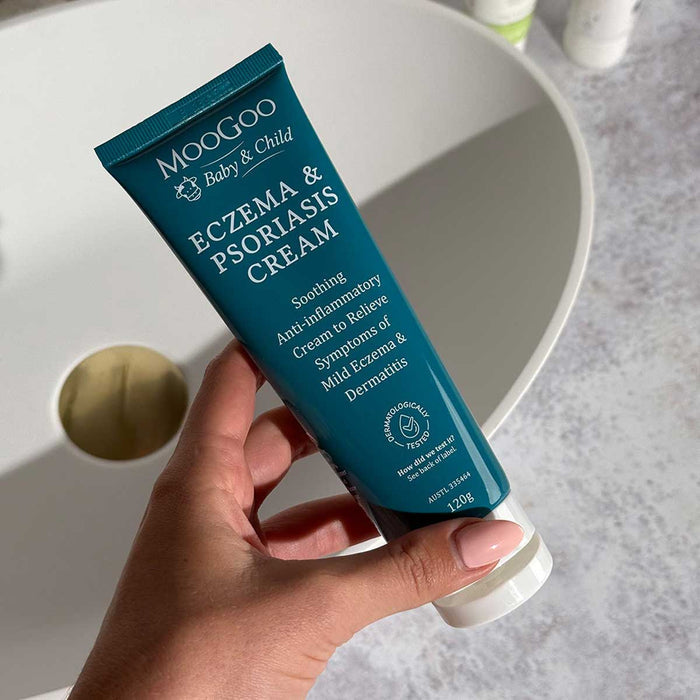 Hand holding a tube of Moogoo Baby & Child Eczema & Psoriasis Cream with a neutral background.