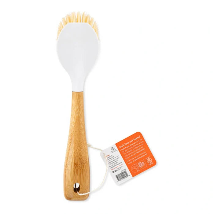 A kitchen scrubber brush with a white silicone head, natural bamboo handle, and a small metal hanging hole. An orange and white product tag is attached to the handle, set against a plain white background.