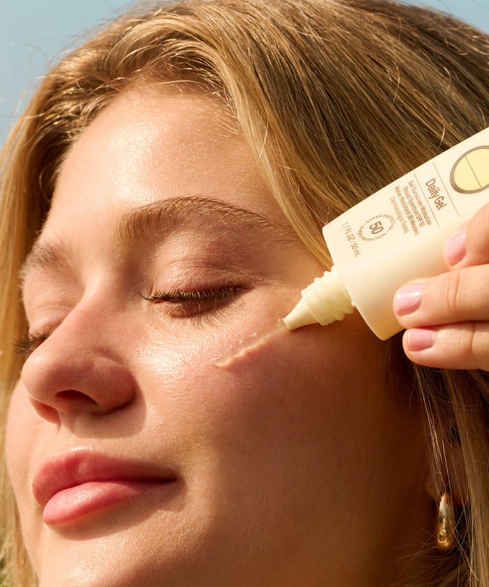 Close-up of woman applying Daily Body + Face Gel Bundle from Sun Bum to her cheek on sunny day