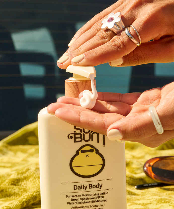 Person dispensing lotion from Sun Bum Daily Body + Glow Bundle bottle onto their hand in bright sunlight