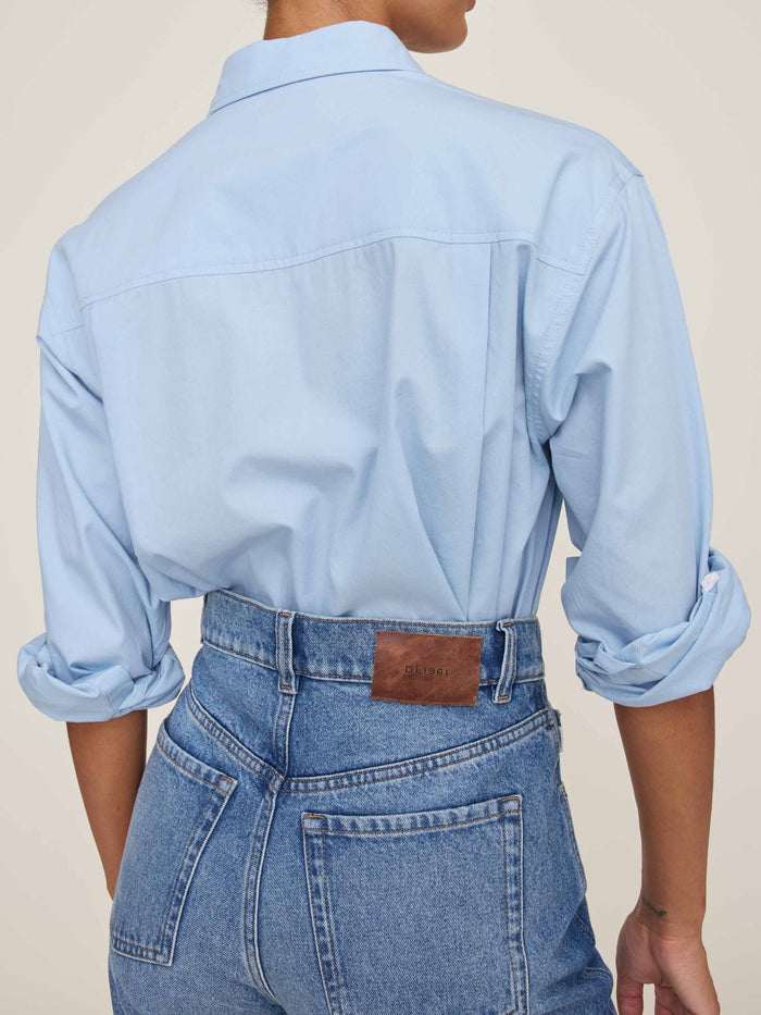Light blue shirt and jeans worn by a person on a beige background