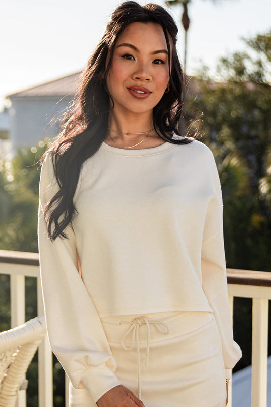Woman wearing a white outfit on a balcony with greenery in the background