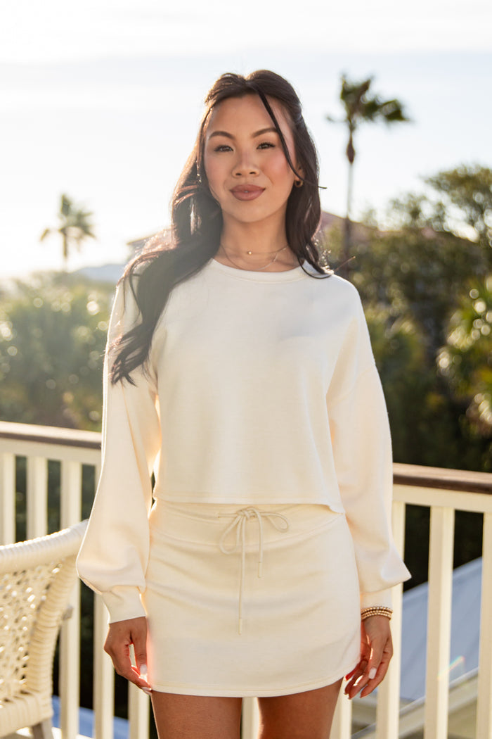 Woman wearing a white outfit on a balcony with greenery in the background