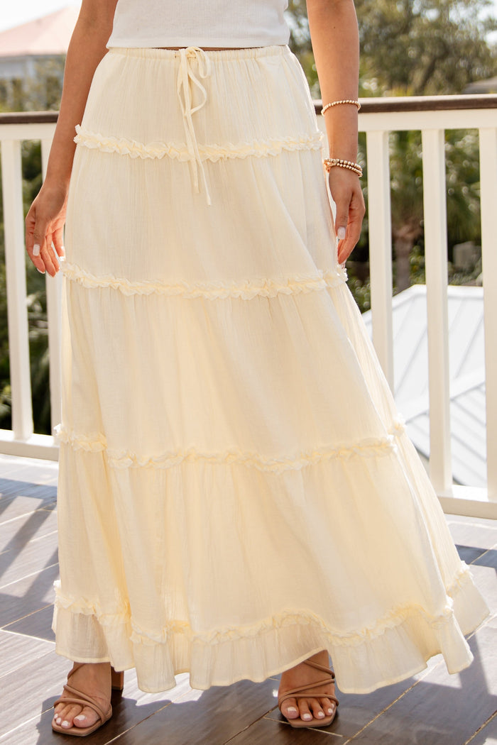 Person wearing a long, light-colored skirt on a balcony.