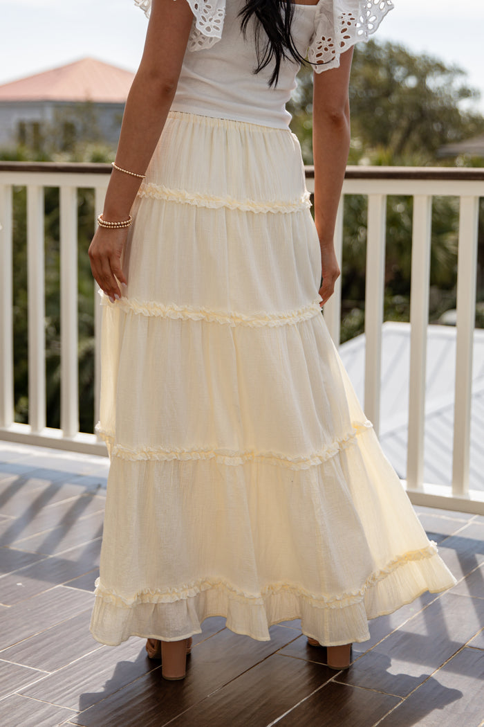 Person wearing a white lace top and cream-colored tiered skirt on a balcony.
