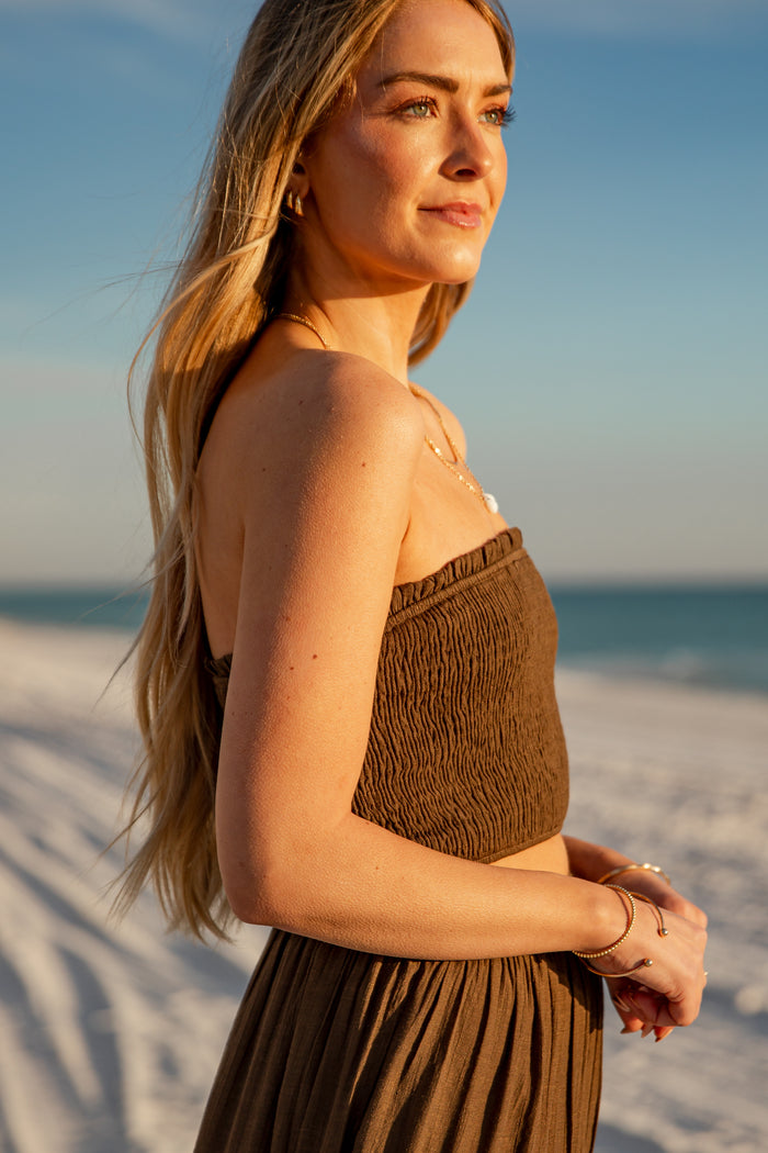 Woman in a brown dress standing on a sandy beach with ocean view