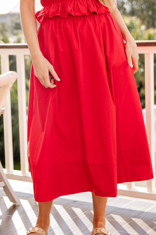 Person wearing a red dress on a balcony with greenery in the background