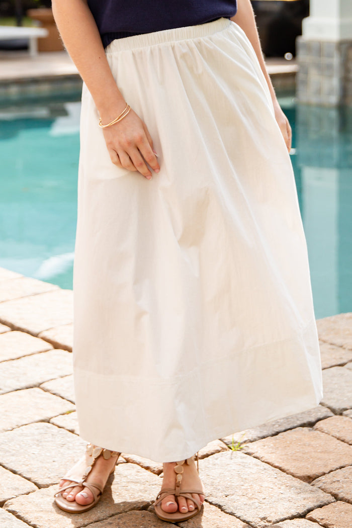 Person wearing a navy top and white skirt by a poolside