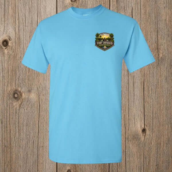 Fort Denaud Beard and Skin sky blue cotton t-shirt with a detailed chest badge graphic on a rustic wood background.
