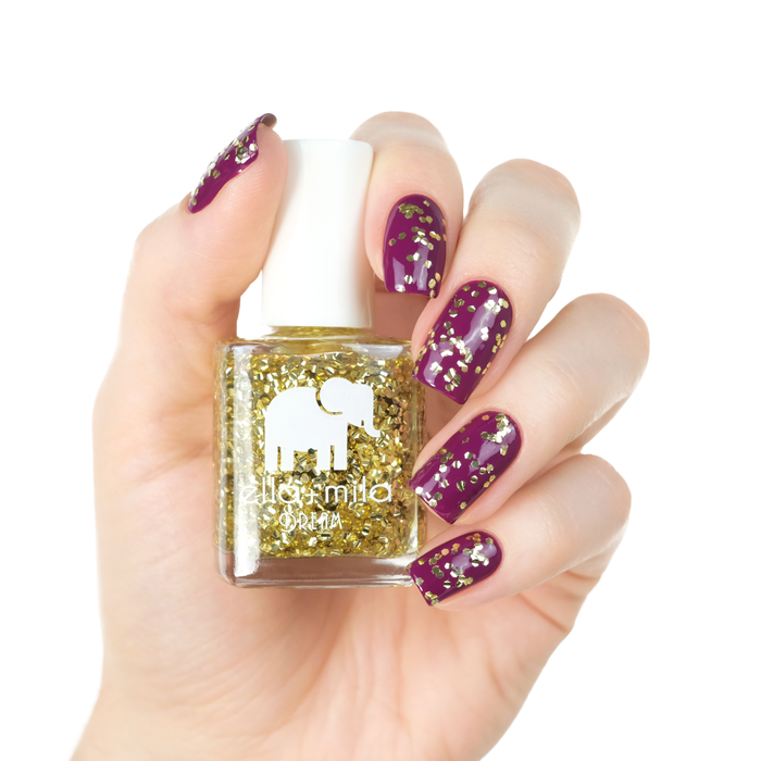 G-Old Money gold glitter nail polish layered over dark polish, holding the bottle