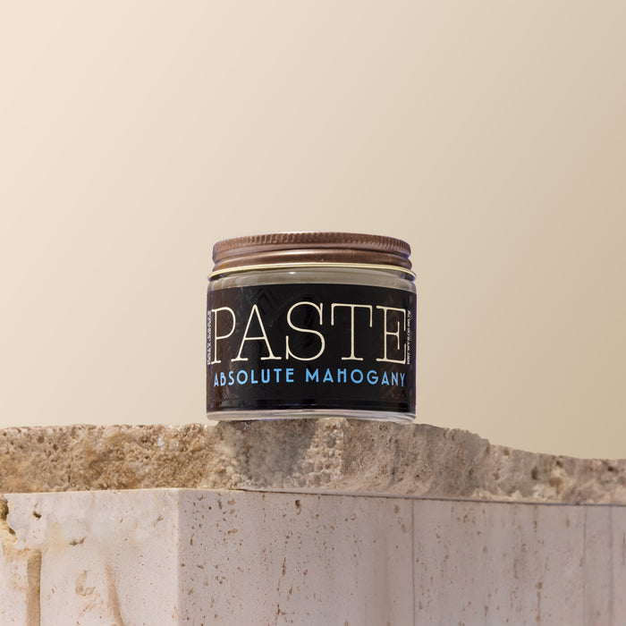 Jar of 'Paste' Absolute Mahogany hair product on a stone surface with a beige background