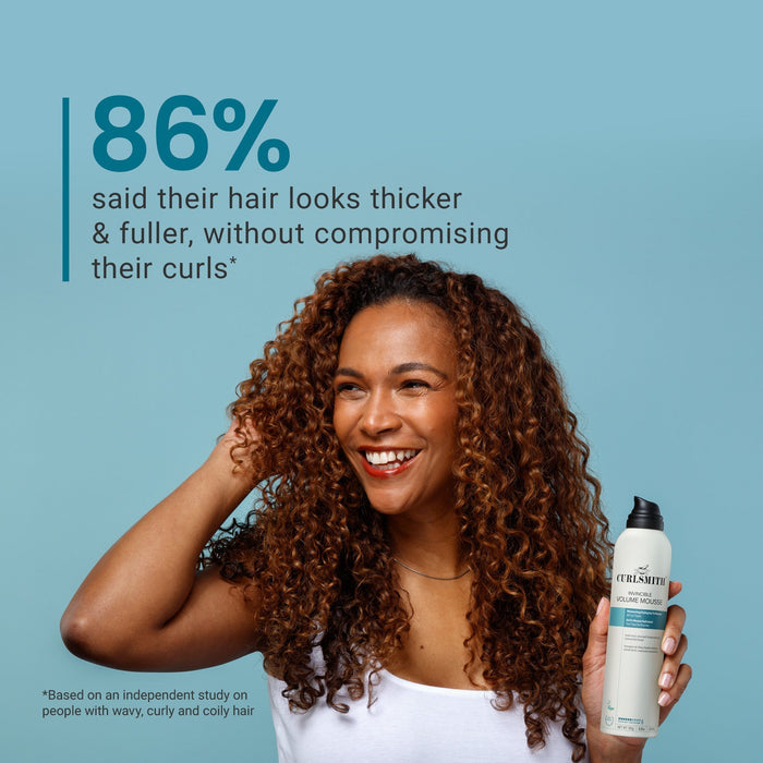 Woman with curly hair holding a bottle of product against a blue background