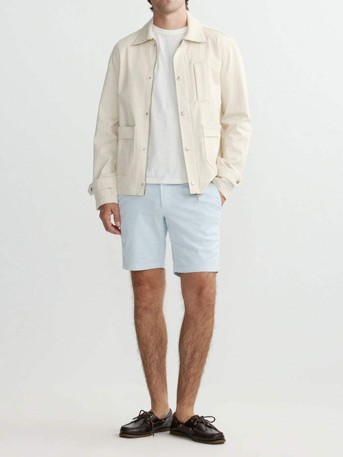 Man wearing a light-colored shirt, shorts, and jacket on a white background