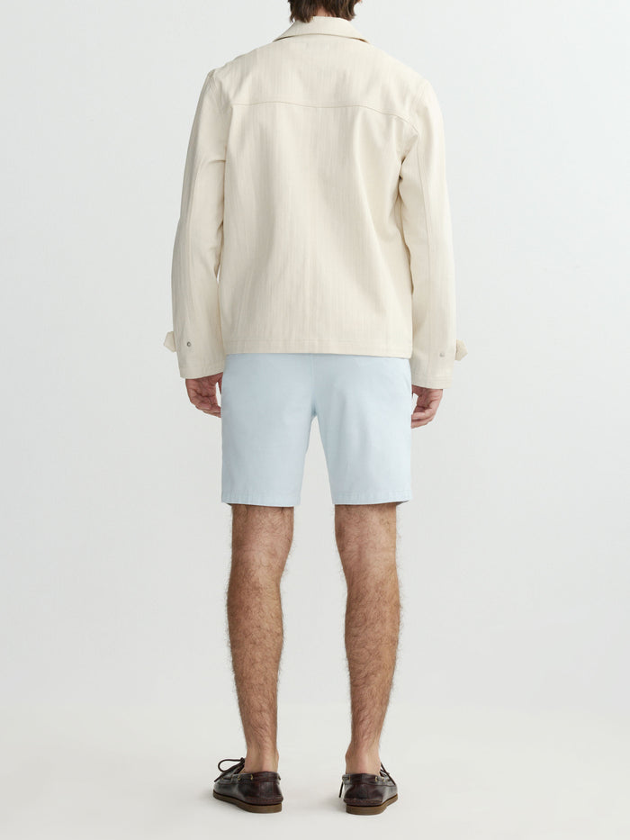 Person wearing a light-colored jacket and light blue shorts on a white background
