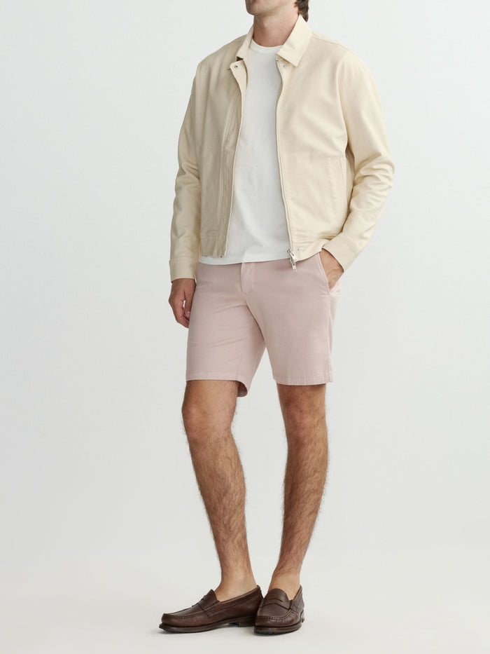 Man wearing a beige jacket, white shirt, and pink shorts on a light gray background