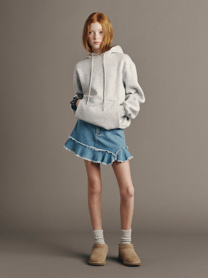 DL1961 girls' Jenny ruffle-hem mini skirt in light blue 'Unraveled' with a grey hoodie, full-length front view.