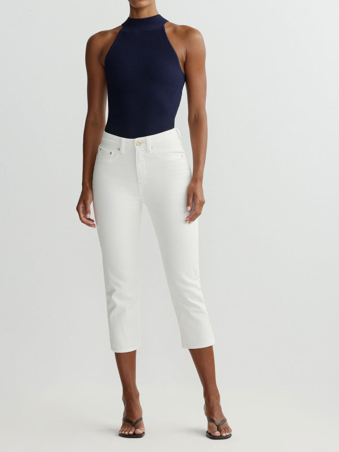 Person wearing a navy sleeveless top and white pants on a light gray background