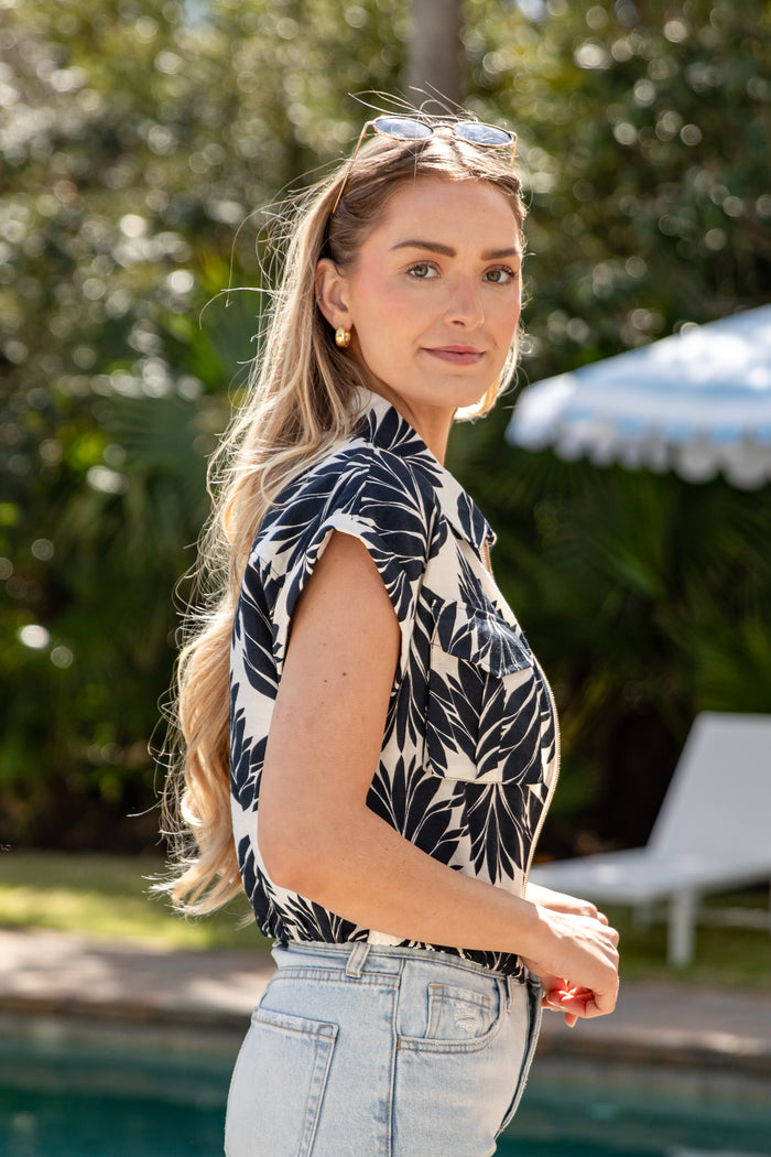 Woman in a patterned top and jeans standing by a pool with greenery in the background
