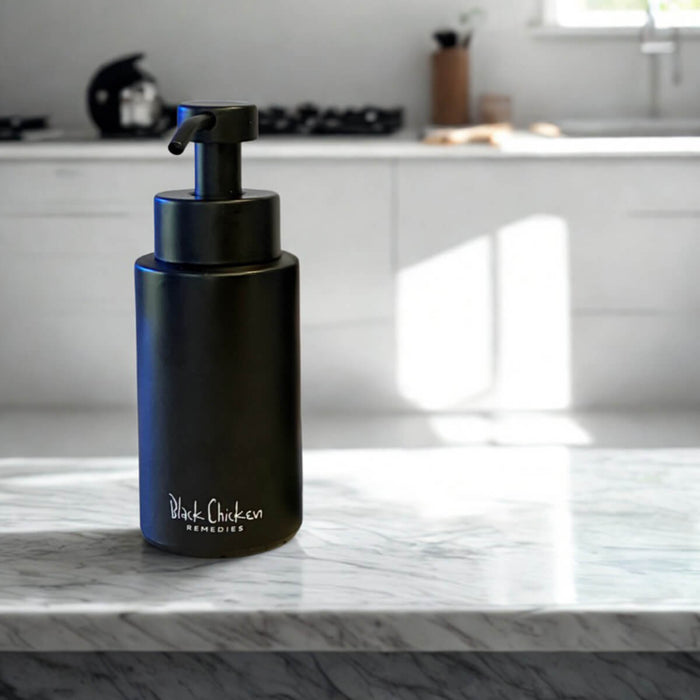 Black Chicken Remedies PureFoam Glass Soap Dispenser on a countertop.