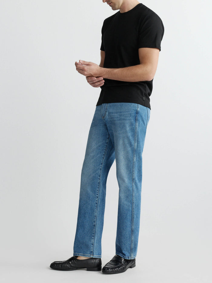 DL1961 men's ribbed crewneck tee in black 'Black', three-quarter side full-length with blue jeans.