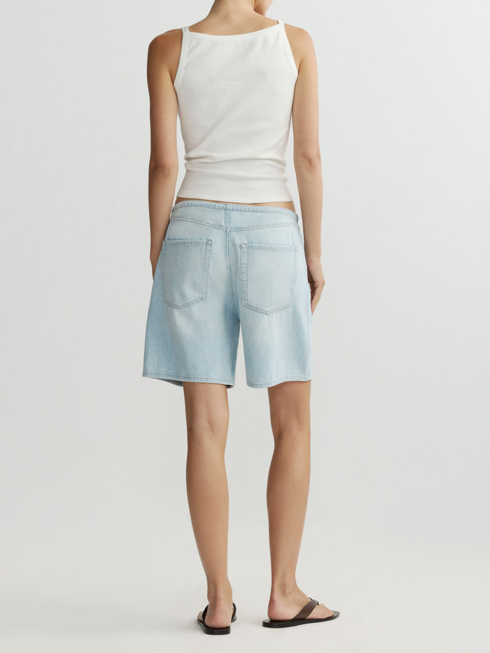 Person wearing a white sleeveless top and light blue denim shorts on a plain background