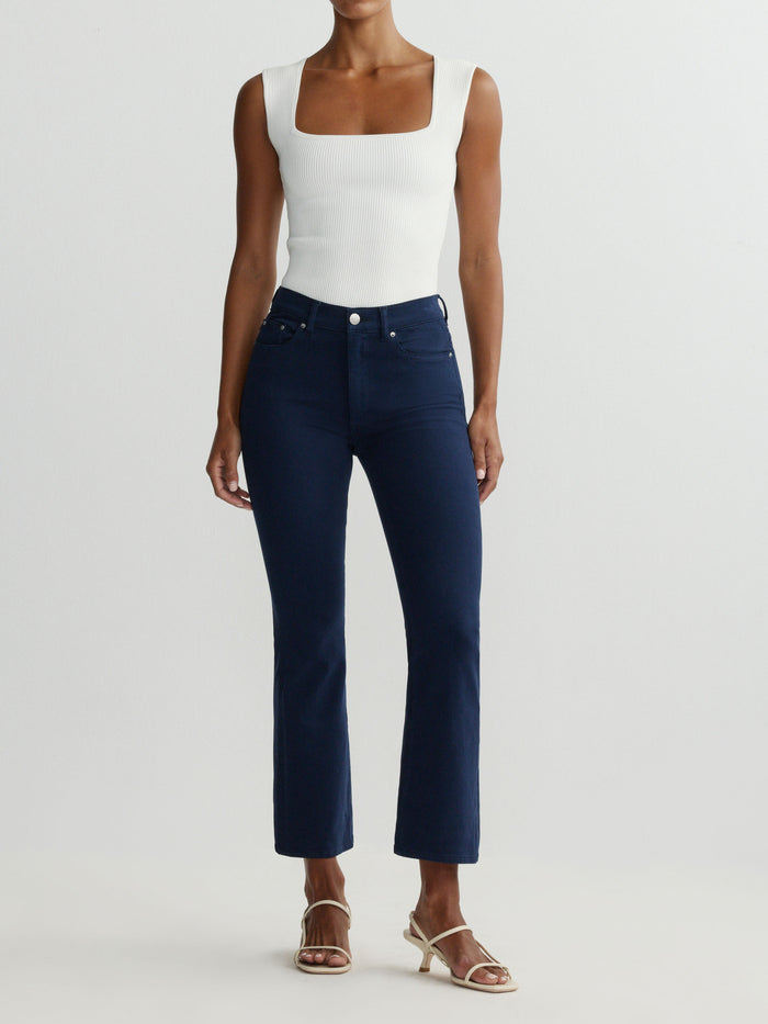 Person wearing a white sleeveless top and dark blue jeans on a light gray background