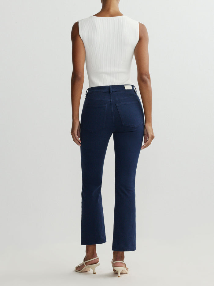 Person wearing navy pants and a white top on a light gray background