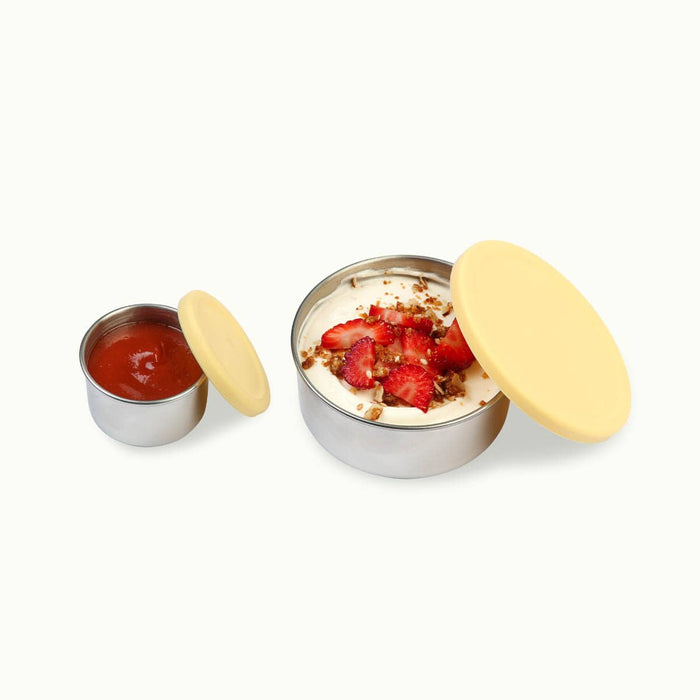 Buttercup yellow silicone lids and stainless steel snack pods. Small size filled with sauce. Bigger size filled with yoghurt, strawberries & granola.