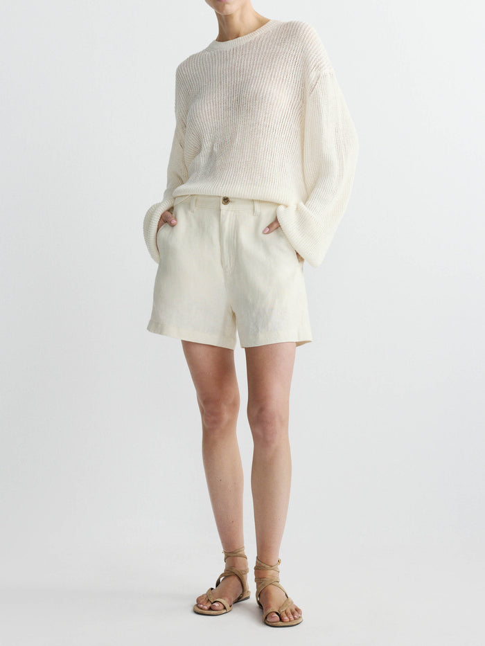 Person wearing a cream sweater and linen shorts set on a white background