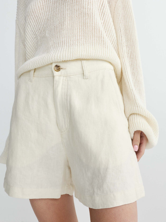 Person wearing a cream sweater and linen shorts set on a white background
