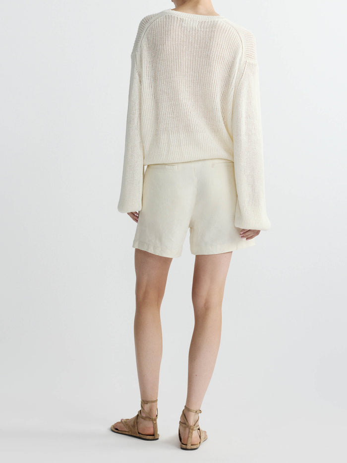 Person wearing a cream sweater and linen shorts set on a white background