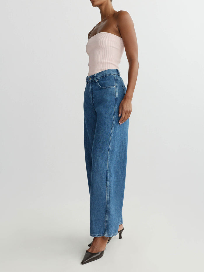 Woman wearing blue jeans and a light pink top on a plain background