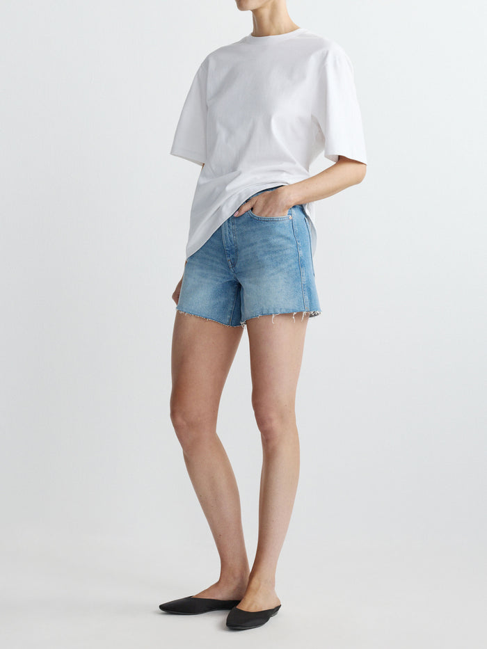 Person wearing a white t-shirt and blue denim shorts on a plain background