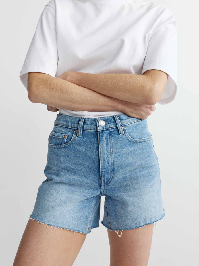Person wearing light blue denim shorts and a white t-shirt on a plain background