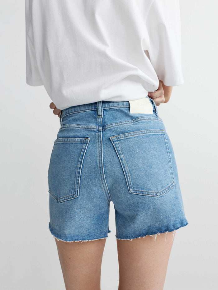 Person wearing blue denim shorts and a white sweatshirt on a plain background